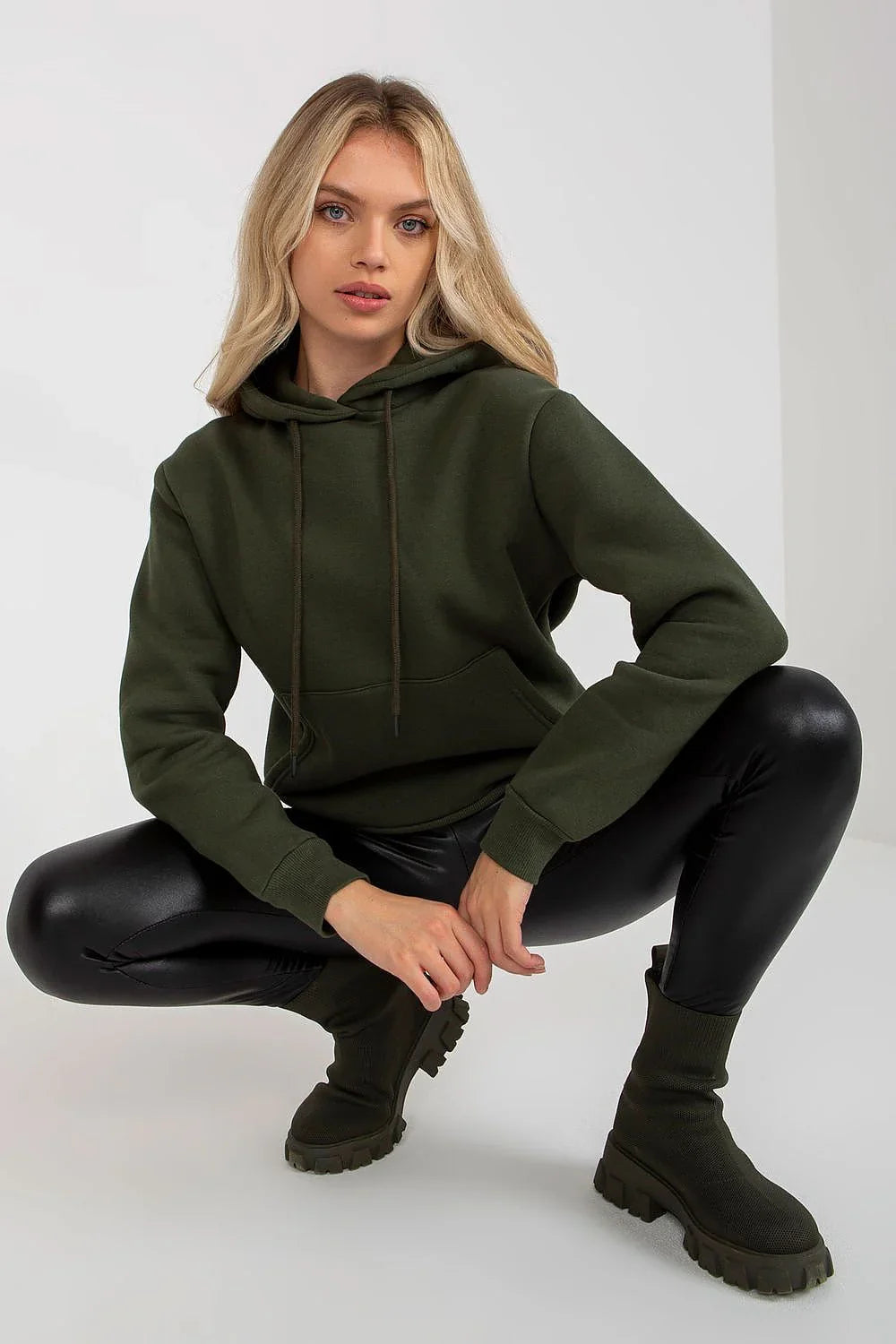 Woman crouching in an olive green pullover hoodie and black leggings fashion image